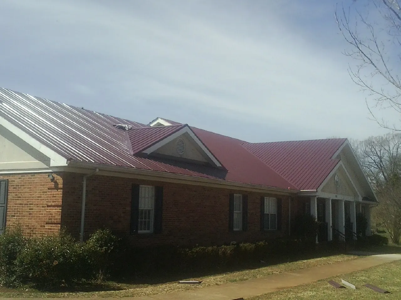 Red metal roof with gabled entries on a long brick building, from a Hail Damage Roof Repair job in Dakota City