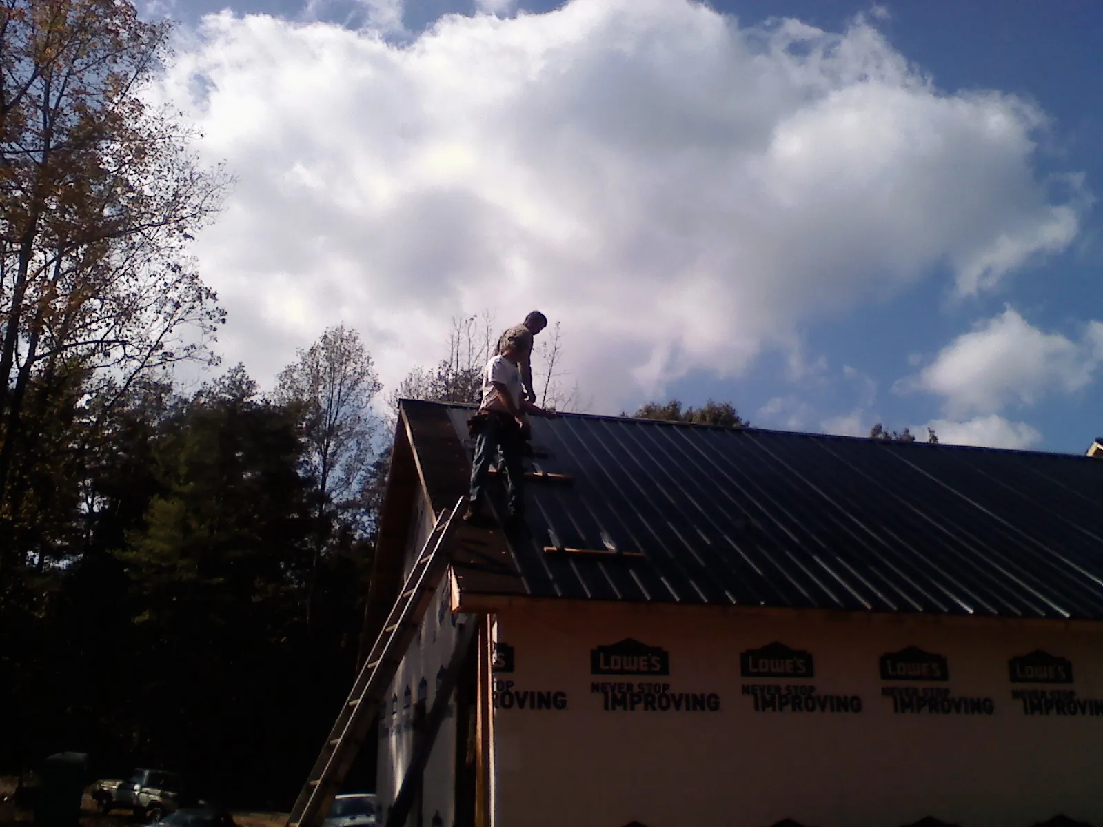 Roofer fastening dark metal panels high against a cloudy sky, from a Roof Inspection job in Dakota City