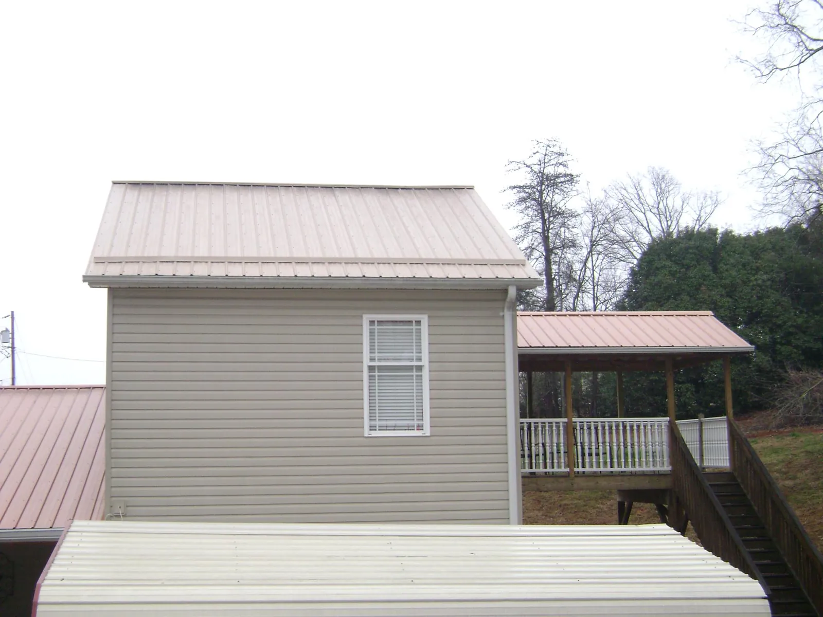 Tan metal roofs on a two story addition and attached porch, from a Roof Replacement job in Dakota City