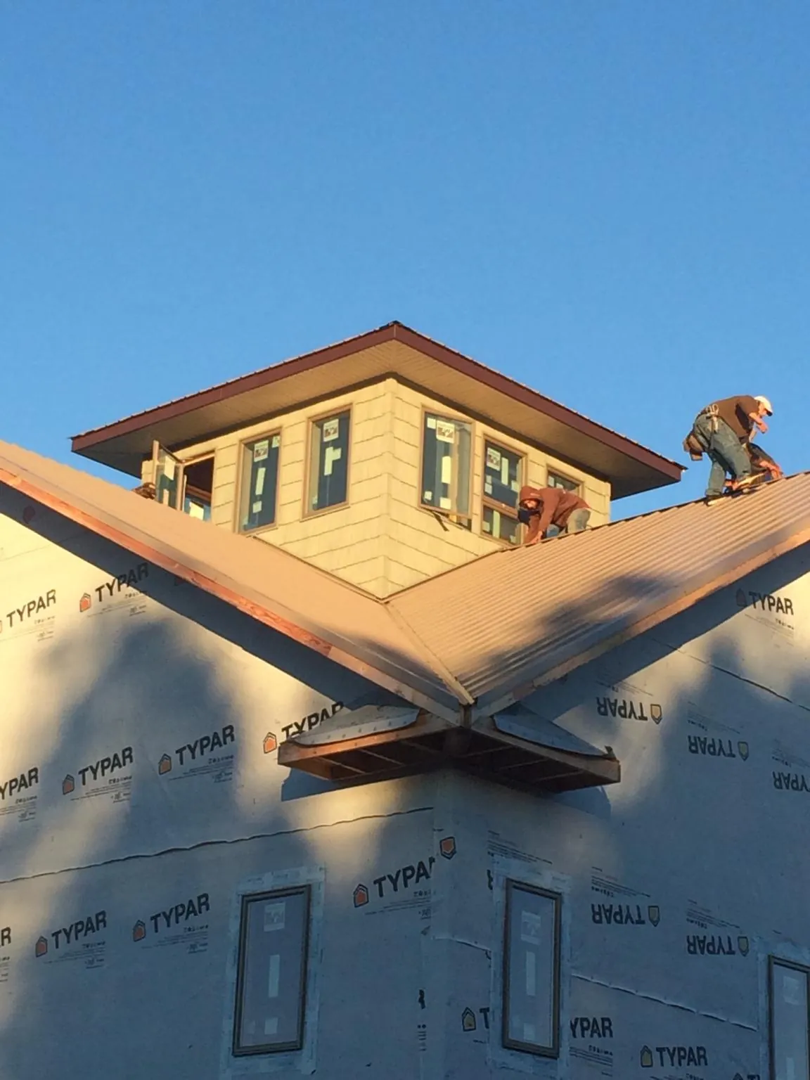 Roofers working around a rooftop cupola on a new metal roof at sunset — Roof Waterproofing in Dakota City by Roofing Brothers
